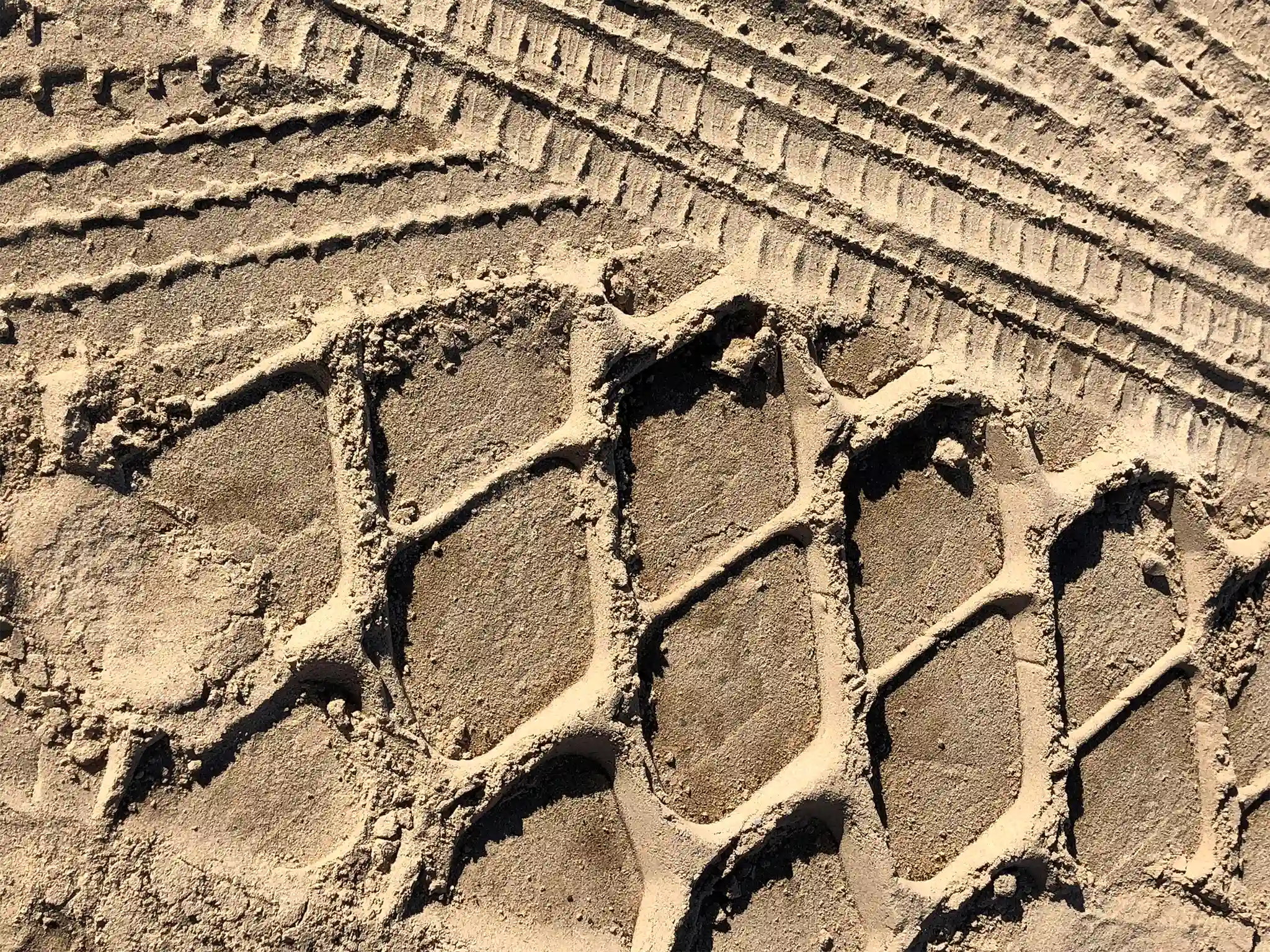 Tire tracks left in sand by trucks and heavy equipment.