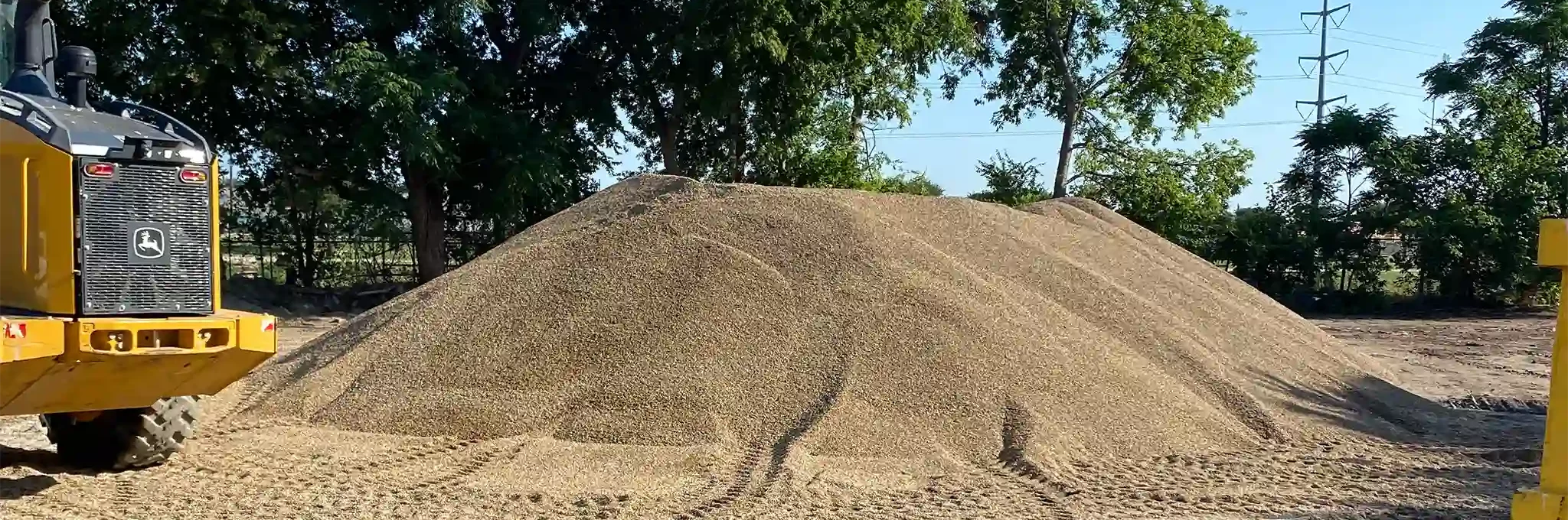 A large pile of 3/8" pea gravel is stored outside with yellow loaders nearby.