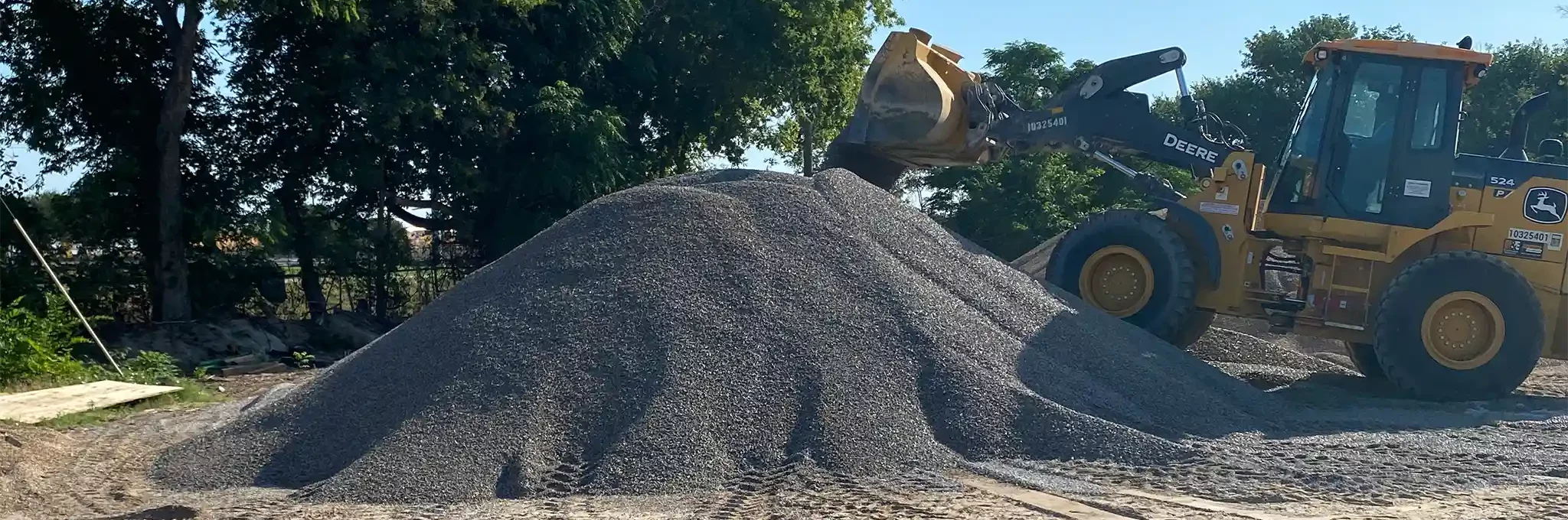 A yellow loader adds to a large pile of 1" utility stone.